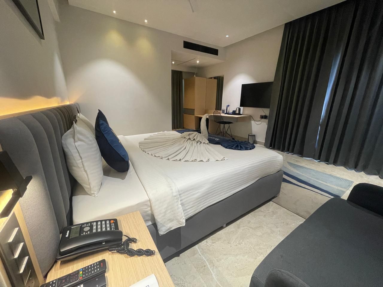 Bedroom at Hotel Kyzen HiTech City with a king bed, side table and curtained windows.
